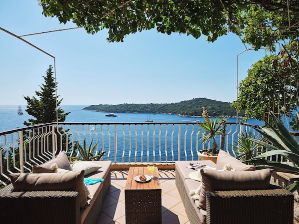 A terrace with wicker furniture, a table, and a view of the sea and a distant island. - Hedera Estate, Hedera A17 (Dubrovnik)