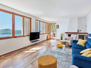 A spacious living area with a large TV, a blue sofa, and a view of the sea. - Hedera Estate, Hedera A17 (Dubrovnik)