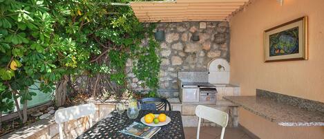 Un patio exterior con una mesa, sillas, una parrilla y un muro de piedra.