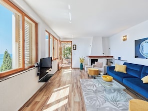 A spacious living room with a large TV, a blue sofa, and a view of the sea. - Hedera Estate, Hedera A17 (Dubrovnik)