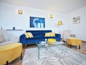 A living room with a blue sofa, a yellow armchair, a glass coffee table, and a floor lamp.