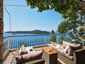 A terrace with wicker furniture, a table, and a view of the sea and a distant island.