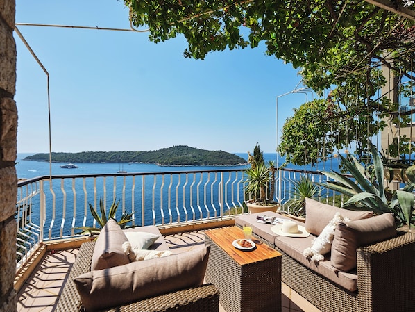 A terrace with wicker furniture, a table, and a view of the sea and a distant island. - Hedera Estate, Hedera A17 (Dubrovnik)