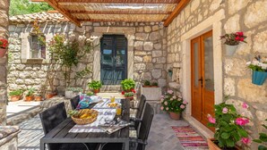 A stone building with a wooden door, potted plants, and a table set for dining. - Summer Cottage (Dubrovnik)