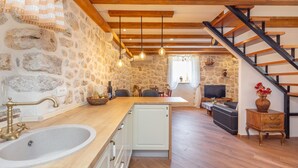 A kitchen with a stone wall, wooden beams, a large sink, and a staircase leading to another room. - Summer Cottage (Dubrovnik)