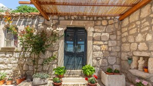A stone building with a wooden door, potted plants, and a small statue. - Summer Cottage (Dubrovnik)