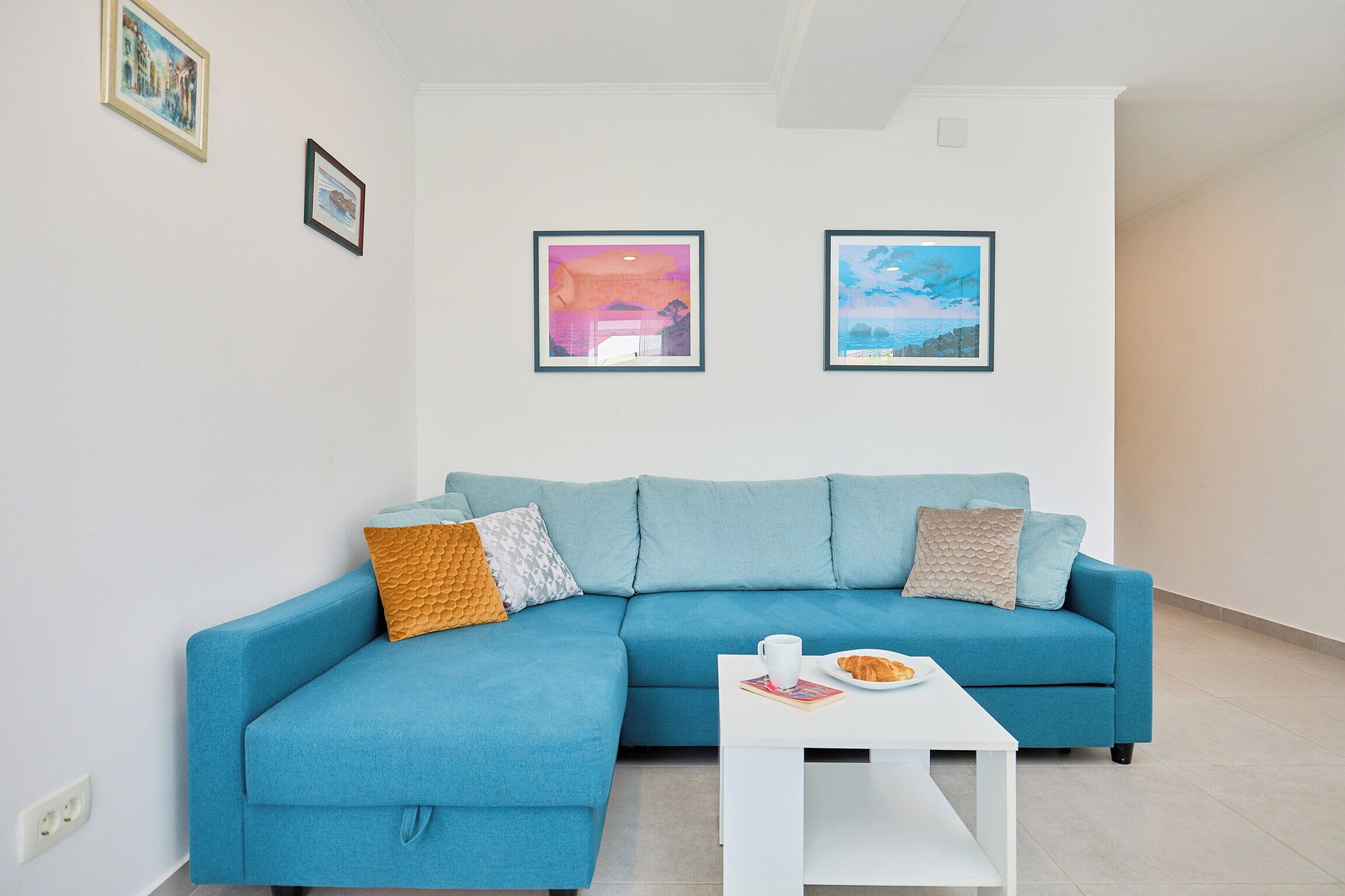 Un salon moderne avec un canapé d’angle bleu, une table basse blanche et deux tableaux encadrés accrochés au mur.