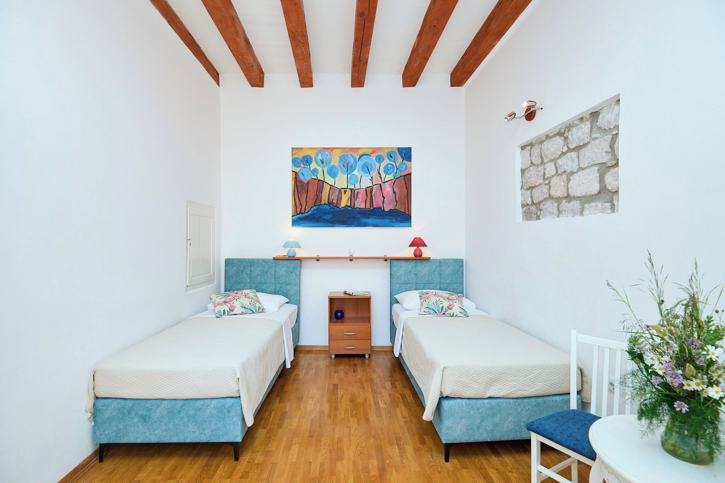 Une pièce avec deux lits, une petite table, une chaise, un tableau et un mur en pierre.