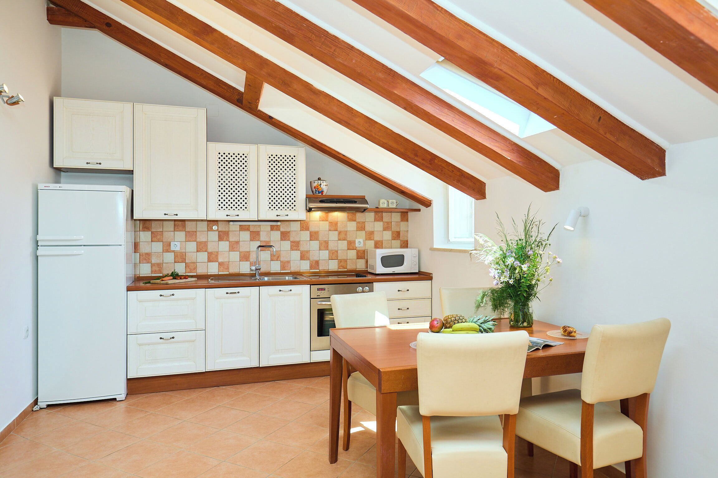 Cucina con mobili bianchi, un forno a microonde, un lavandino e un'area pranzo con tavolo e sedie.
