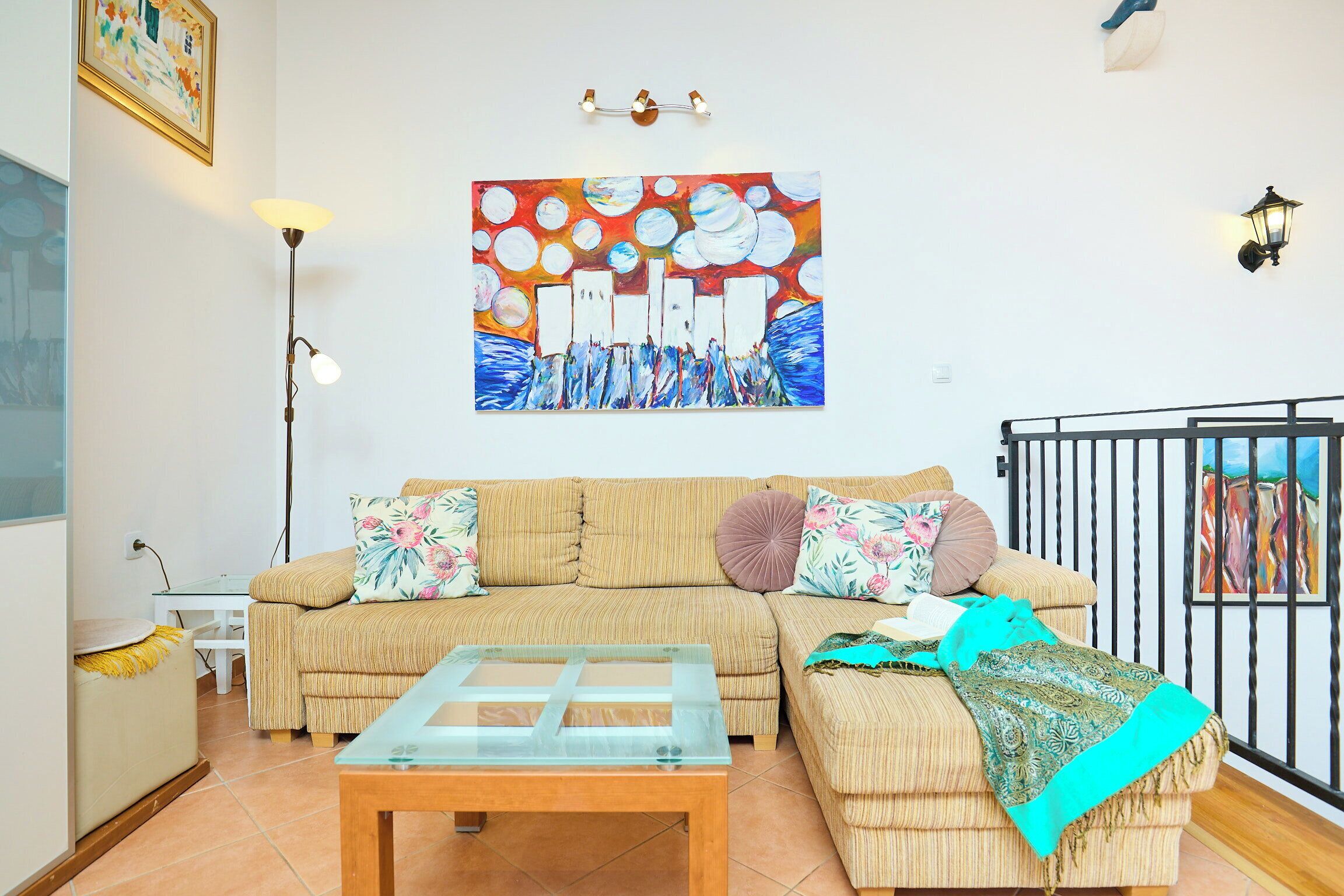 Uma sala de estar com sofá, mesa de centro de vidro, um quadro na parede e um corrimão.