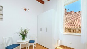 A room with a white wardrobe, a small table with a vase, two chairs, and a window with a view of a tiled roof. - Hedera Estate, Hedera A34 (Dubrovnik)
