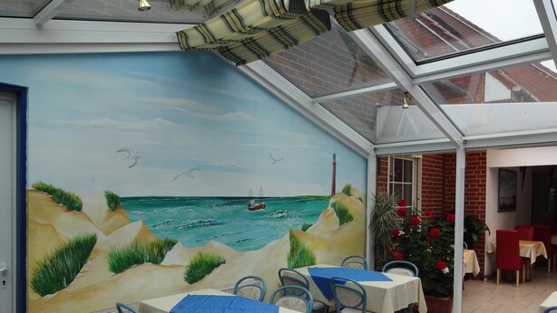 Un restaurante con un mural de paisaje marino, mesas con manteles azules y sillas.