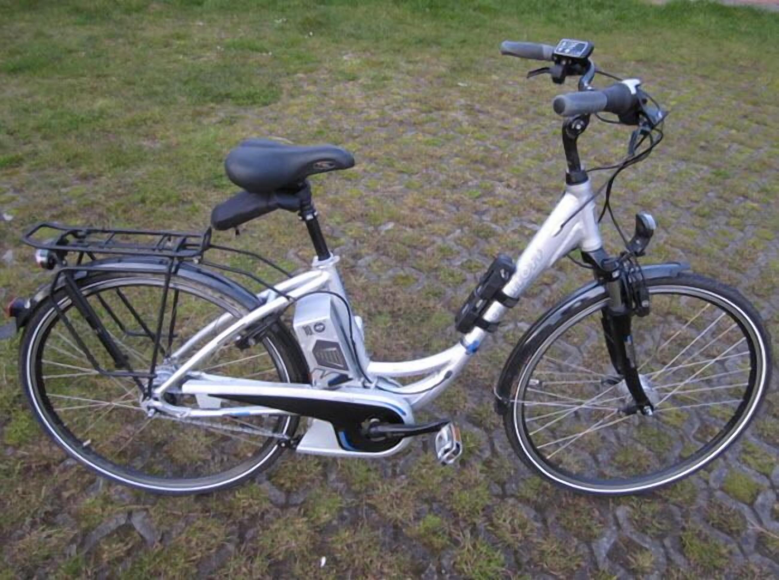 Ein stationäres Fahrrad mit schwarzem Sattel und Korb vorne, abgestellt auf Pflastersteinen.