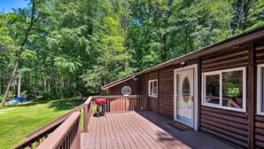 A wooden deck with a barbecue grill, a covered seating area, and a view of a forested area. - Hike, Hunt & Unwind: Cozy Cabin Near Hersheypark (Jonestown)