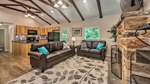 A spacious living area with a fireplace, leather sofas, and a kitchen in the background. - Hike, Hunt & Unwind: Cozy Cabin Near Hersheypark (Jonestown)