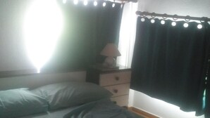 Une chambre à coucher avec un lit, une table de chevet, une lampe et une fenêtre avec des rideaux.