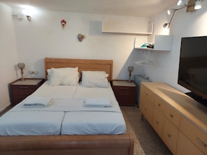A neatly arranged hotel room with a double bed, bedside tables, a dresser, a TV, and a wall-mounted shelf. - INDIGO TLV (Tel Aviv)