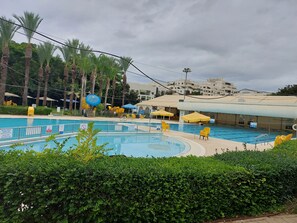 A swimming pool with yellow chairs and umbrellas, surrounded by palm trees and a hedge. - INDIGO TLV (Tel Aviv)