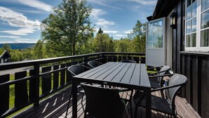 An outdoor deck with a table and chairs, overlooking a scenic landscape with trees and a distant view of mountains.