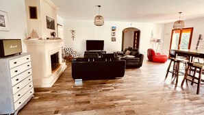 A spacious living room with a fireplace, a black sofa, a red bean bag, and a dining area with a table and chairs.