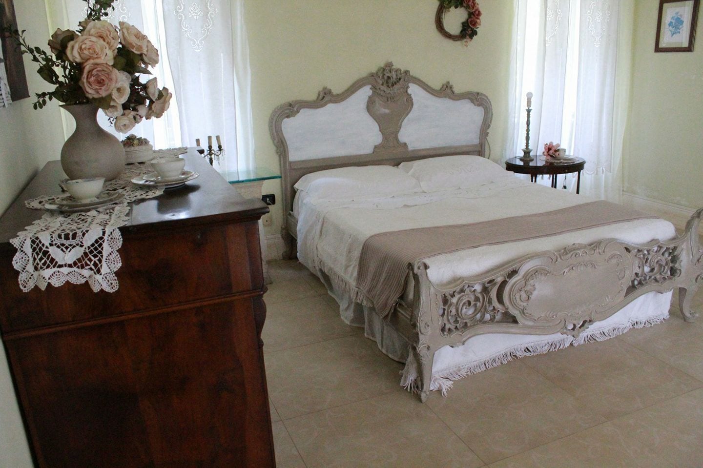 Un dormitorio con una cama grande, un aparador de madera, un jarrón de flores y un adorno colgante en la pared.