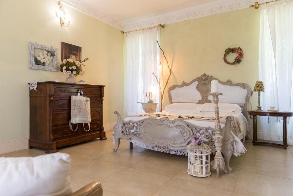 Un dormitorio clásico con una cama grande y decorativa, un aparador de madera y una silla blanca.
