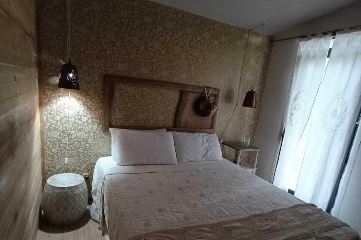 A bedroom with a wooden headboard, a round bedside table, a bed with white linens, and a hanging light fixture.