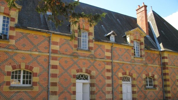 Un bâtiment dont la façade est ornée de briques disposées en motifs, avec de nombreuses fenêtres et une cheminée.