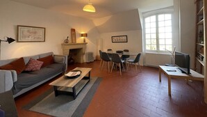 Un salon chaleureux avec un canapé, une table basse, une cheminée, une table à manger avec des chaises et un téléviseur posé sur un meuble en bois.