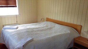 A single bed with a wooden headboard, a bedside table, and a window with blinds. - Frændgardur (Skagafjörour)