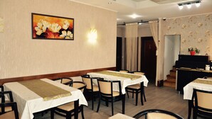 A dining area with tables set for service, a piano, and a wall-mounted light fixture.