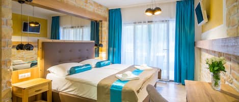 A hotel room with a stone wall, a bed with blue accents, a wooden desk, and a mirror.