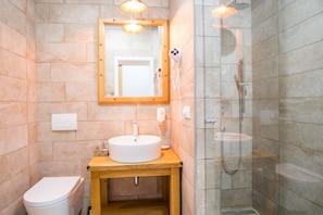 A bathroom with a wooden vanity, a white sink, a mirror, a handheld hairdryer, and a glass-enclosed shower.