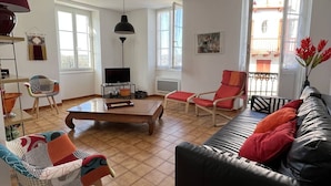A living room with a black leather sofa, red and patterned chairs, a wooden coffee table, and a TV on a stand.