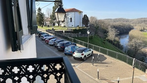 A parking area with cars, a white building with a red roof, and a river in the background.