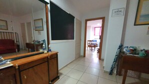 A hallway with a wooden cabinet, a large mirror, and a tiled floor. There is a dining area with chairs and a table in the background. - Doramas Private Rooms Shared Toilet (San Bartolomé de Tirajana)