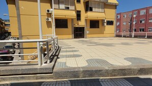 A parking area with a yellow building in the background, a metal railing, and patterned pavement. - Doramas Private Rooms Shared Toilet (San Bartolomé de Tirajana)