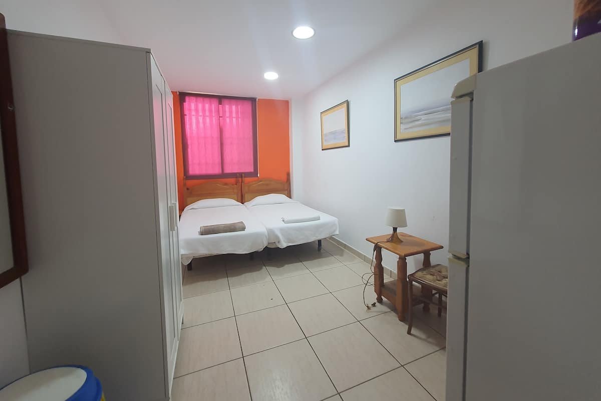 A hotel room with a bed, a small table with a lamp, a window with curtains, and a painting on the wall.