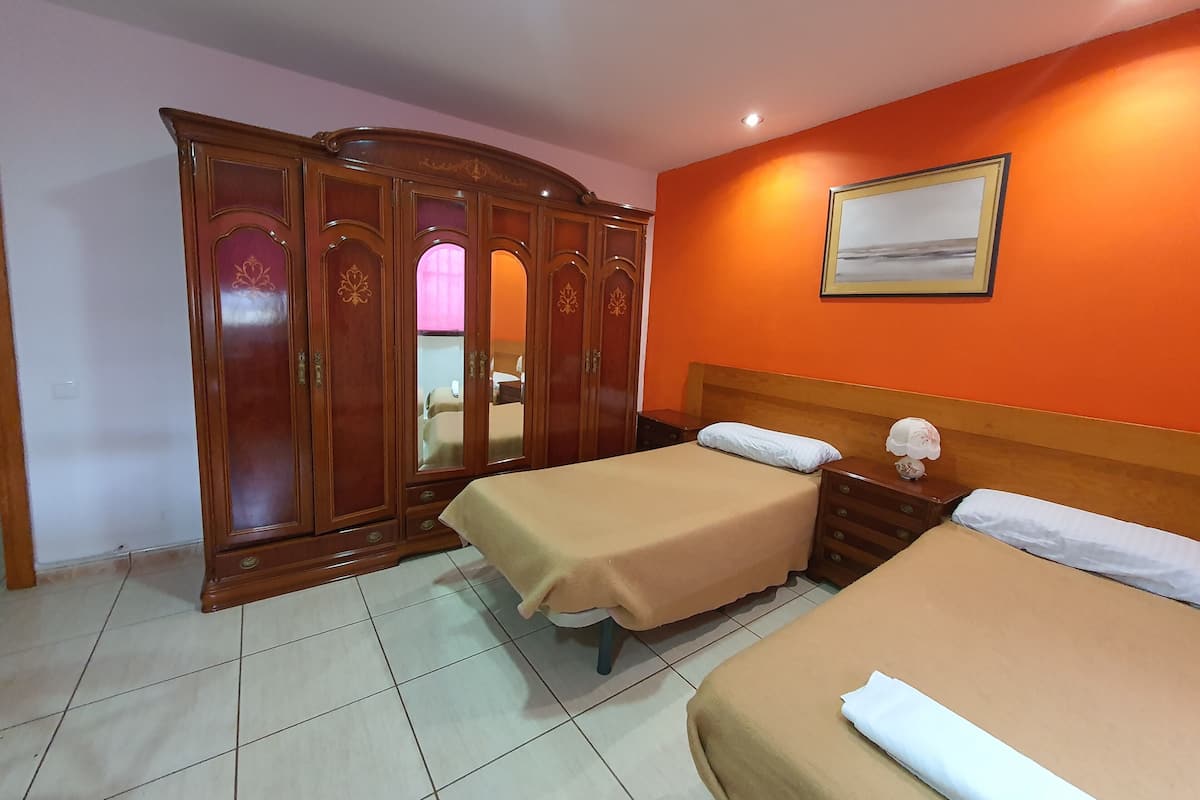 A hotel room with two beds, a wardrobe, and a painting on the wall.