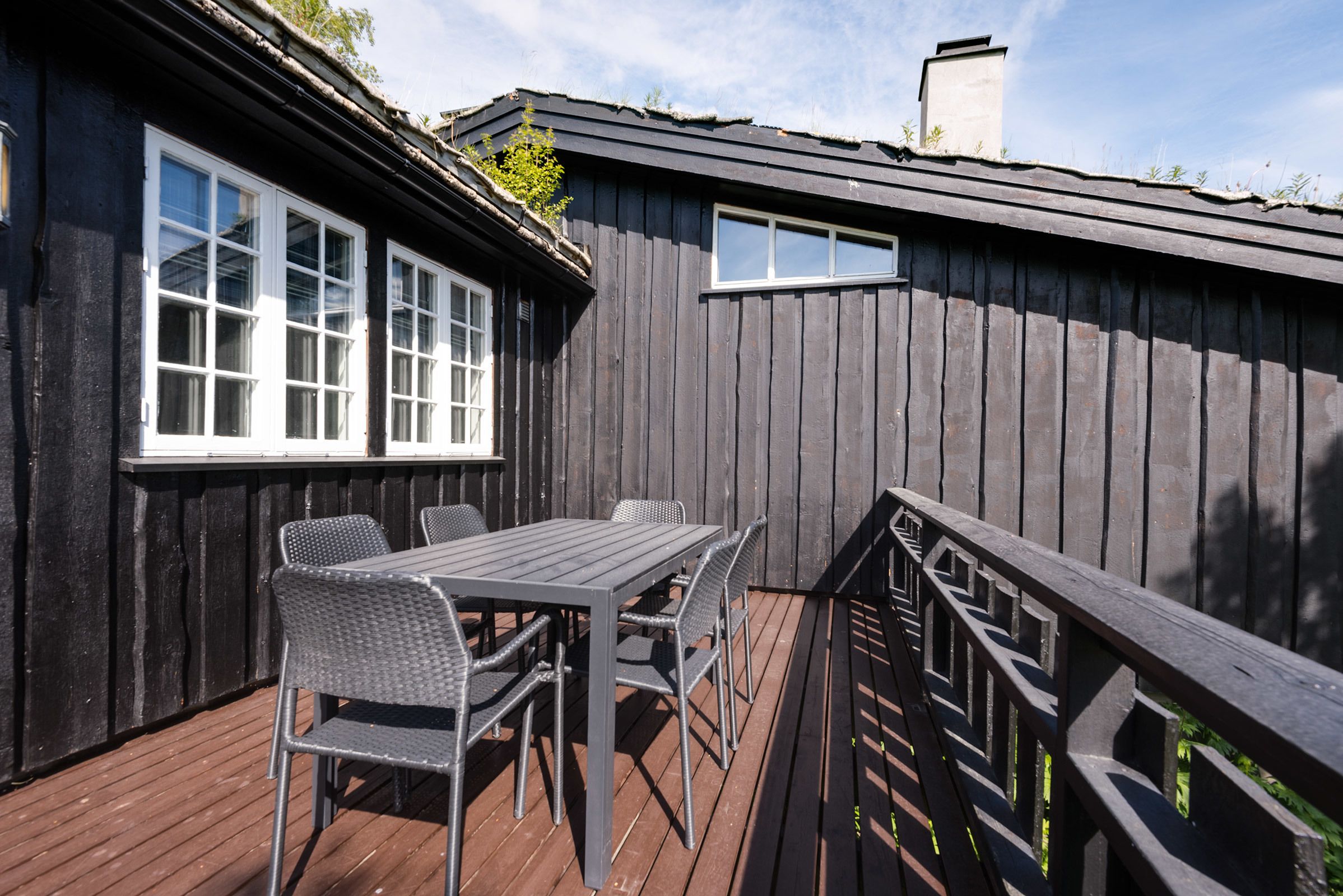 Une terrasse en bois avec une table et des chaises, une rambarde et un bâtiment doté de fenêtres.
