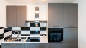 A modern kitchen with black and white checkered backsplash, stainless steel appliances, and grey cabinetry. - Apartments Karolina (Opatija)