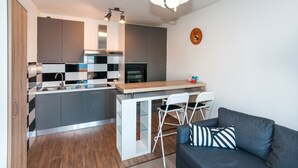 A compact kitchen with a central island, a dining area with chairs, and a sofa with a striped pillow. - Apartments Karolina (Opatija)