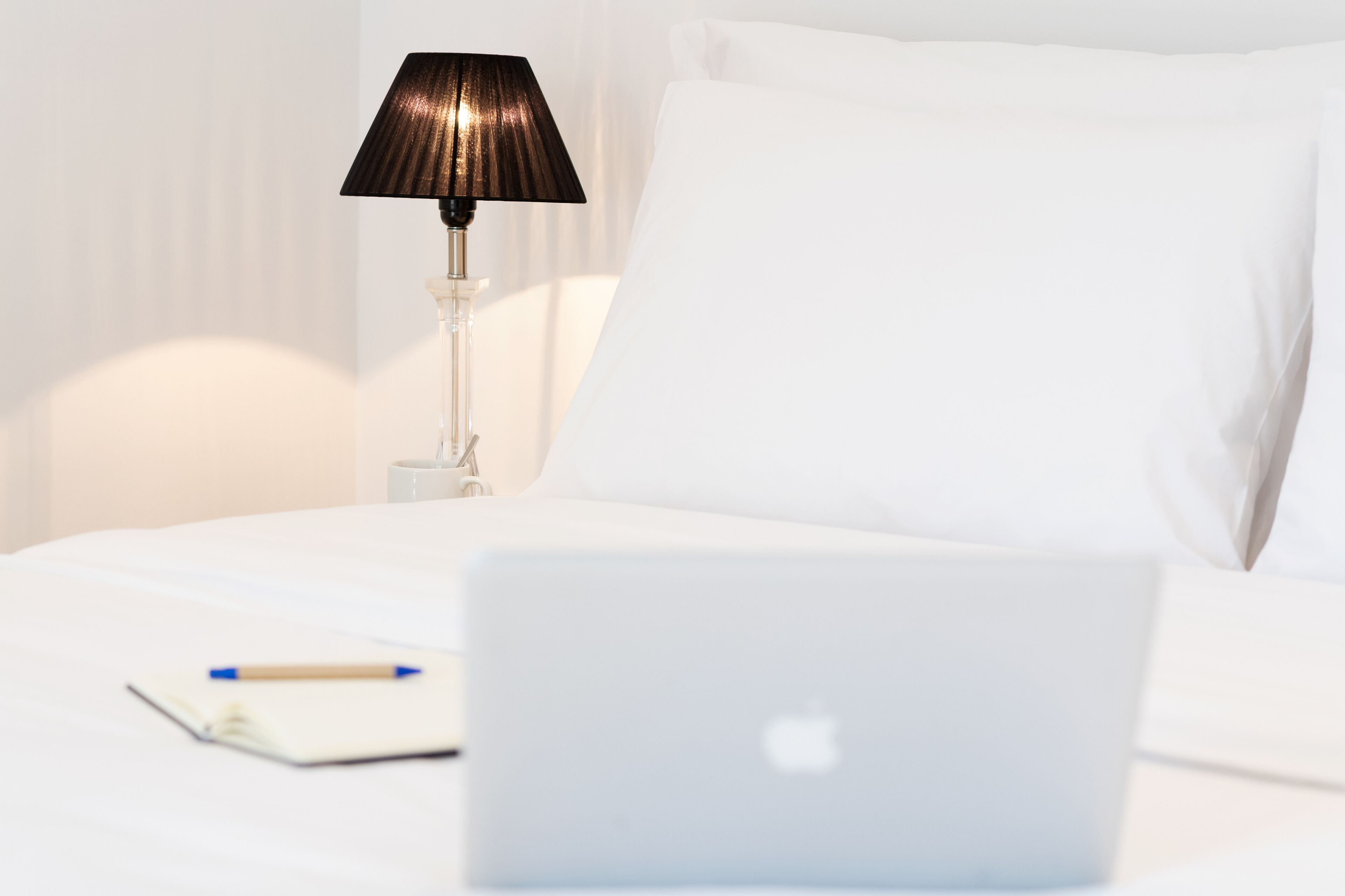 Una cama bien hecha con una laptop, un cuaderno y un bolígrafo encima.