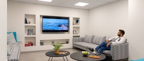 A modern living room with a large flat-screen TV, a sofa, a coffee table, and a small side table with a plant.