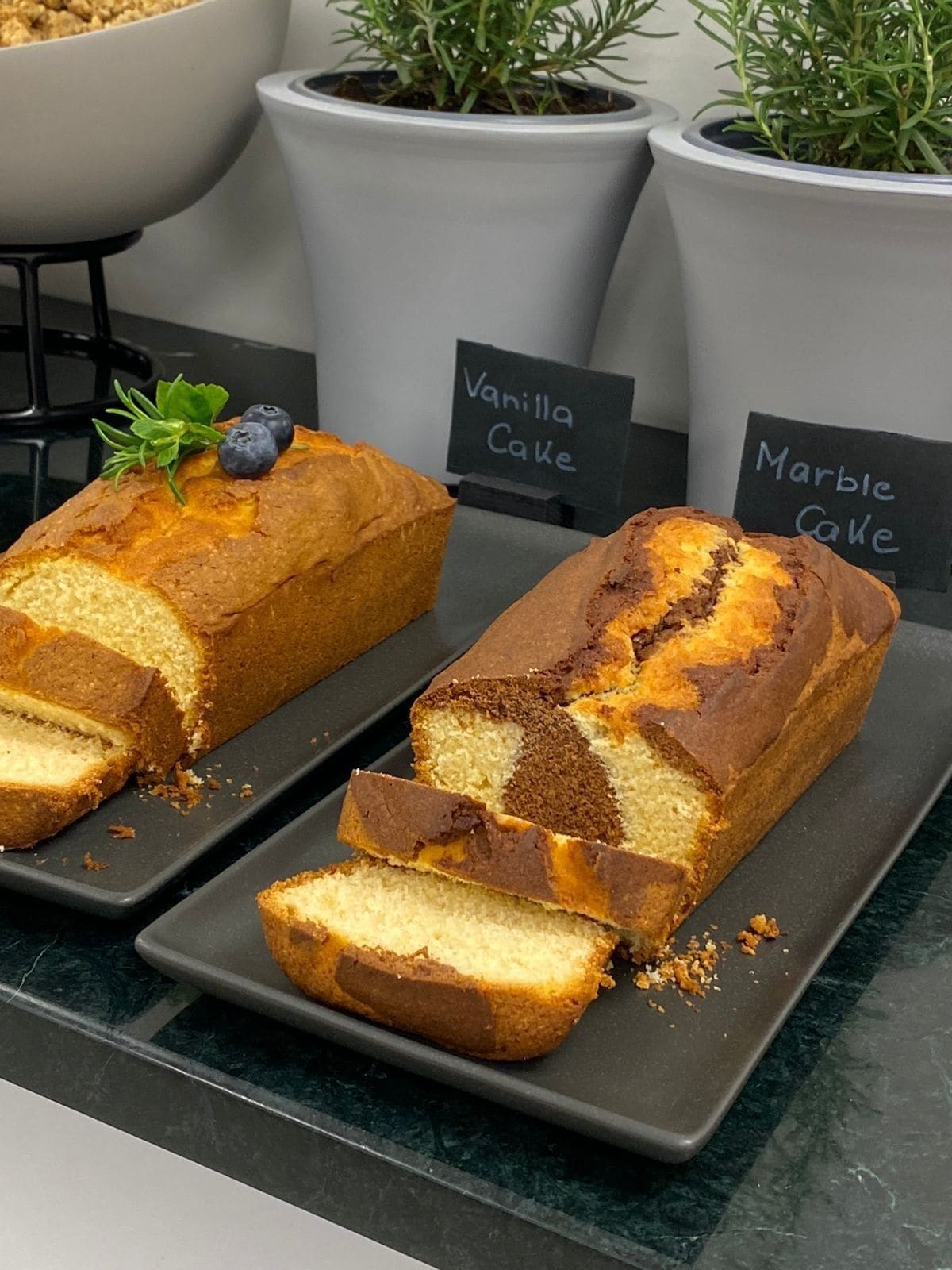 Two loaves of cake on a tray with labels 'Vanilla Cake' and 'Marble Cake'.