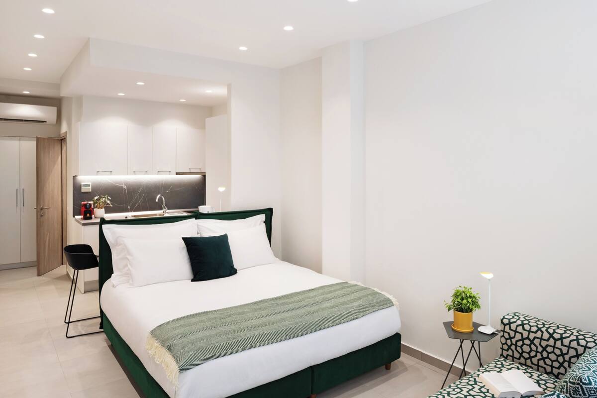 A modern hotel room with a bed, a small desk, a chair, a sofa, and a potted plant.