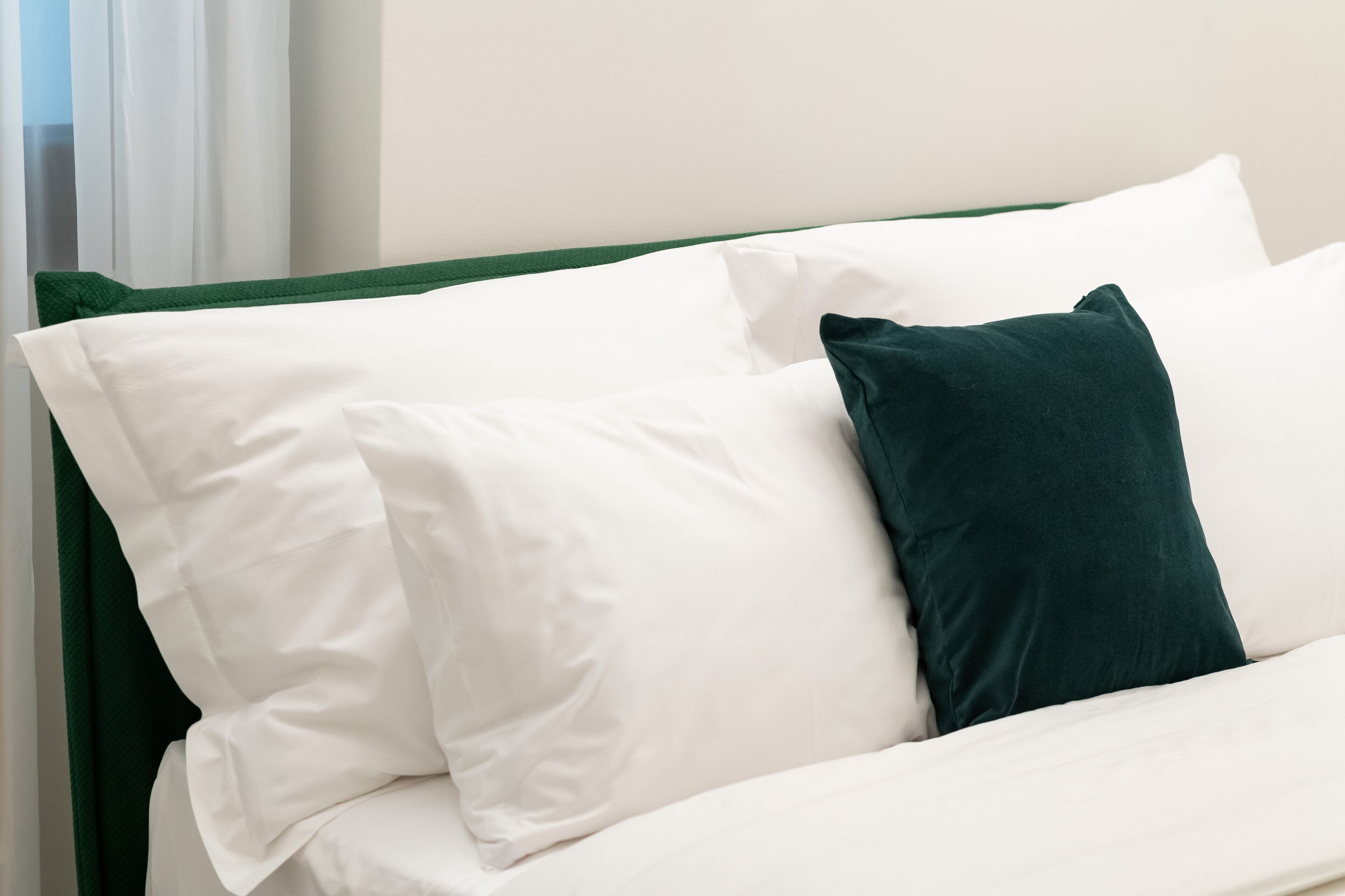 A bed with white and dark green pillows, a green headboard, and a white wall in the background.