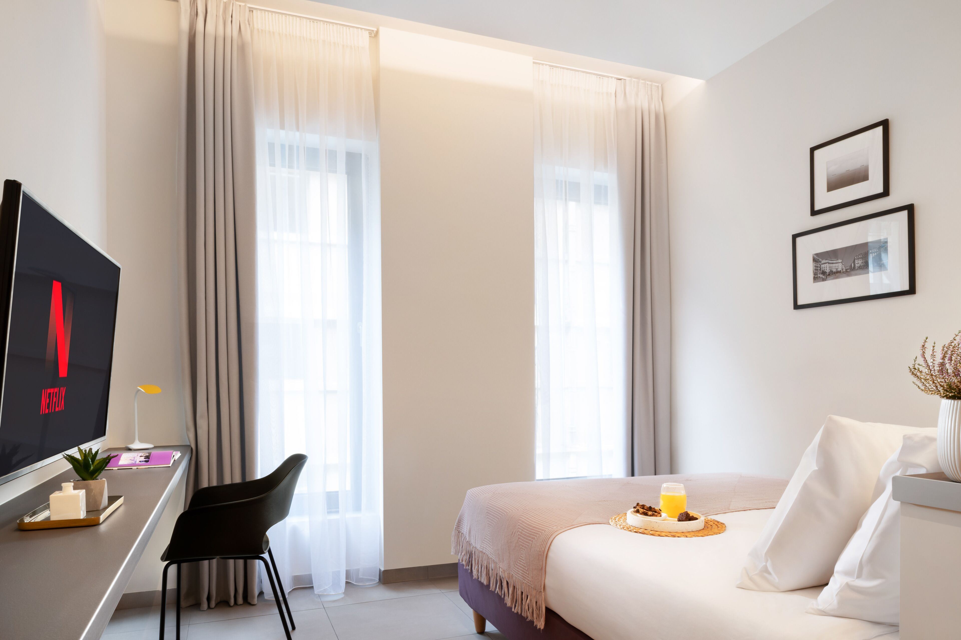 Una habitación de hotel moderna con cama, escritorio con computadora, una silla y ventana con cortinas.