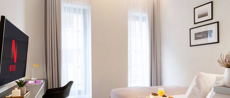Una moderna camera d'albergo con un letto, una scrivania con un computer, una sedia e una finestra con tende.