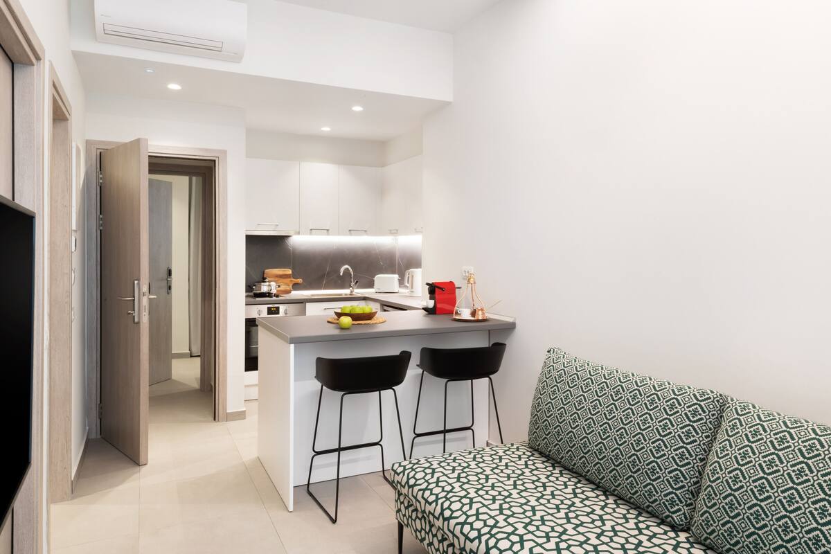 A modern kitchen with a central island, two bar stools, and a patterned sofa.